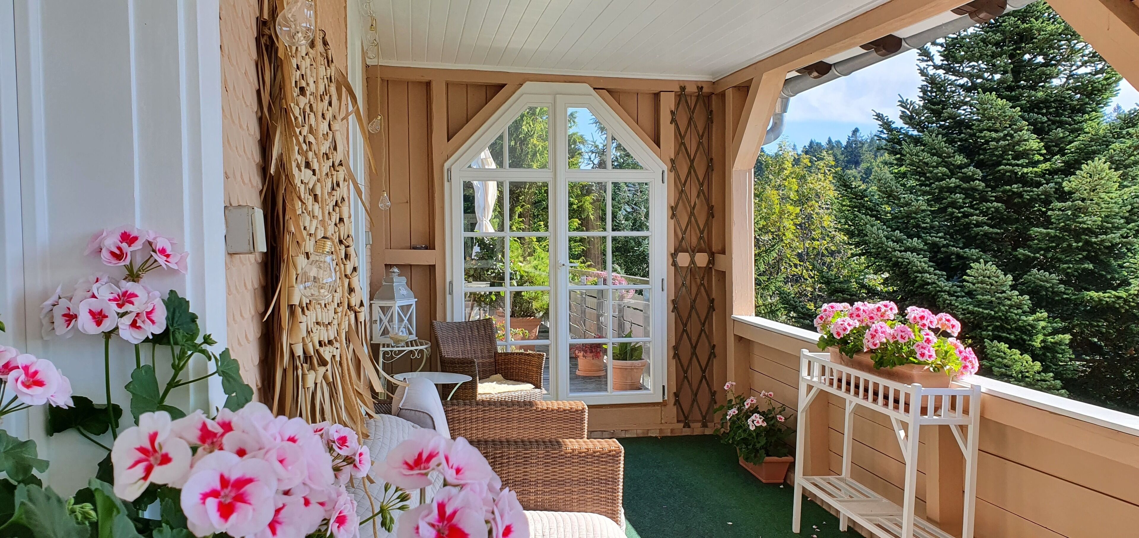 En hyggelig balkon med fletmøbler, en hvid stol og blomsterkrukker.