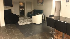 Uma sala de estar com um sofá, uma mesa de centro e uma TV. Há uma porta com a inscrição "APRES SKI" e uma placa com a mensagem "DESCARREGAR AQUI".