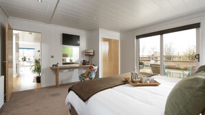 Ein modernes Schlafzimmer mit einem großen Bett, einem Schreibtisch mit Fernseher und einem Balkon mit Sitzgelegenheit.