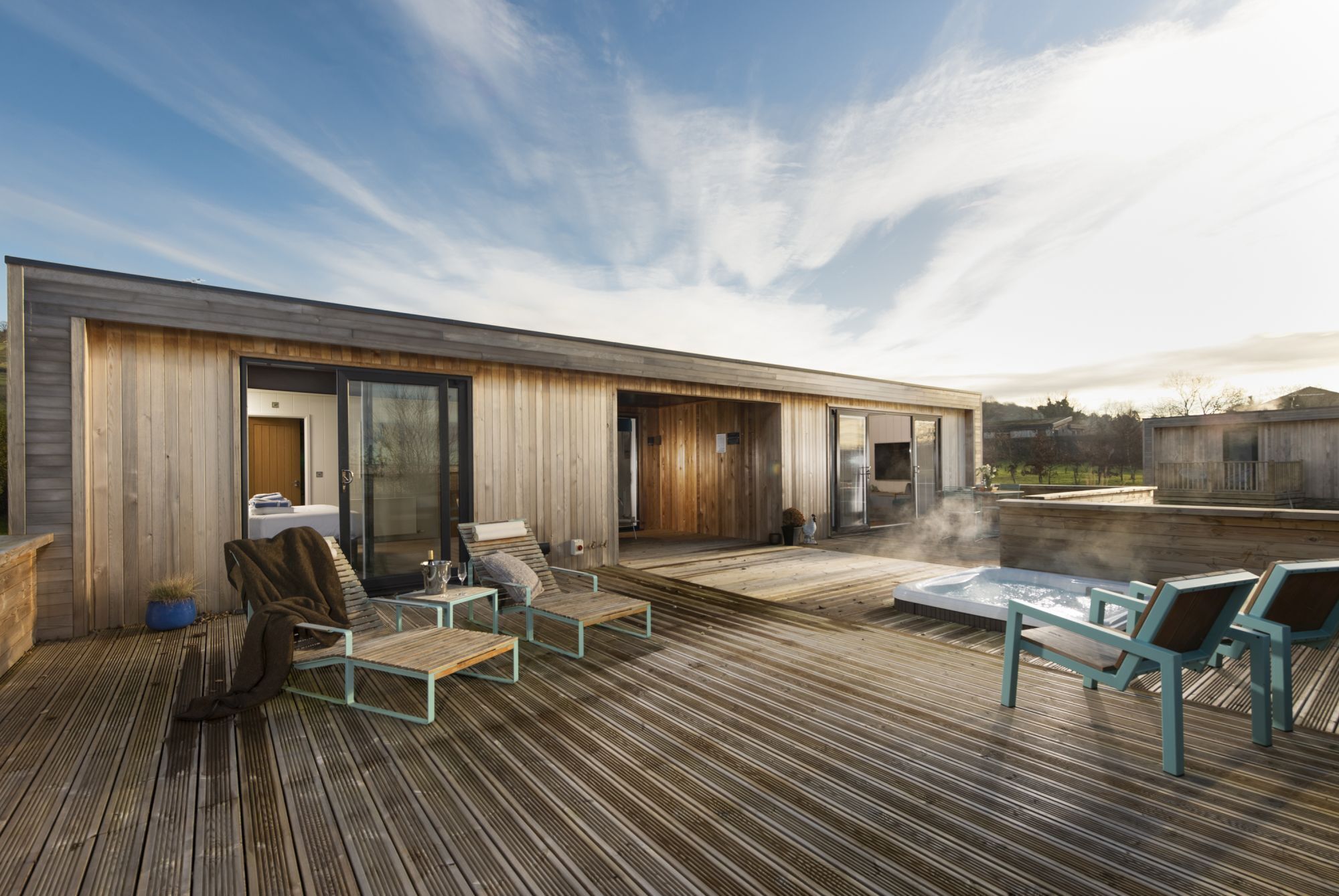 Eine moderne Außenterrasse mit Holzboden, Lounge-Sesseln und einem Whirlpool.