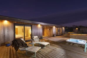 Una terraza moderna al aire libre con un jacuzzi, sillas de descanso y una zona de estar cubierta.