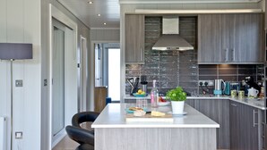 Een moderne keuken met een centraal eiland, donkere houten kastjes en een marmeren achterwand.