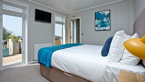 Een slaapkamer met een groot bed, een aan de muur bevestigde televisie en een raam met zonwering.