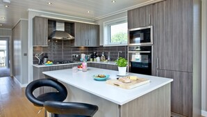 Een moderne keuken met een centraal eiland, roestvrijstalen apparatuur en een zwarte lederen stoel.