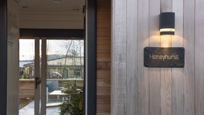 Een houten muur met een bord waarop 'Honeyhurst' staat, en een deur die leidt naar een buitenruimte.