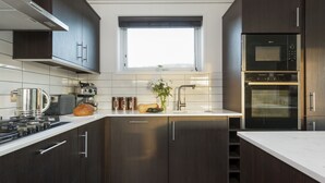 Een moderne keuken met donkerhouten kasten, een roestvrijstalen fornuis, een ingebouwde oven en een raam boven de spoelbak.