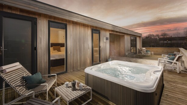 Een wellnessruimte met een jacuzzi, houten terras en lounge stoelen.