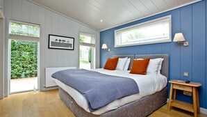 A bedroom with a large bed, a bedside table, a window with blinds, and a picture on the wall.