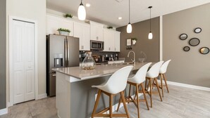 A modern kitchen with white cabinets, stainless steel appliances, and a central island with bar stools. - Storey Lake - LUXURY 4 bedrooms, 3 bath, private pool -  Star Wars & Mickey theme (Kissimmee)