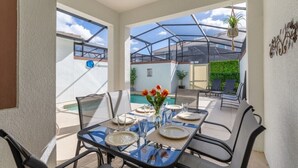 A dining area with a glass table, chairs, and a view of a swimming pool and greenery. - Storey Lake - LUXURY 4 bedrooms, 3 bath, private pool -  Star Wars & Mickey theme (Kissimmee)