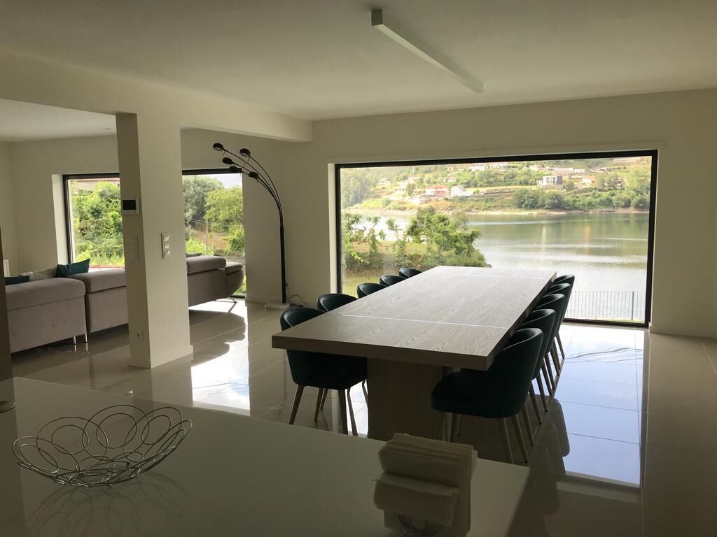 A modern dining area with a large table and chairs, a sofa, and a view of a lake and buildings.