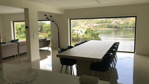 Un comedor moderno con una mesa grande y sillas, un sofá, y vistas a un lago y edificios.
