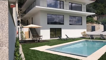 A modern two-story house with a swimming pool, a covered patio, and a staircase leading to the upper floor.