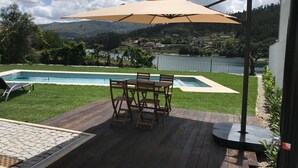 Una terraza de madera con mesa de billar, una mesa de comedor con sillas y un paraguas grande.