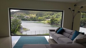 Un moderno salón con un ventanal que ofrece vistas a un lago y la vegetación circundante.