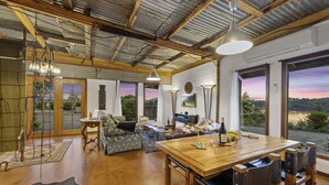 A spacious living area with a wooden dining table, a sofa, and a large window offering a scenic view.