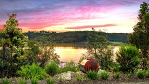 A lakeside view with a sunset, trees, and a barrel.