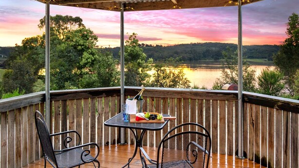 A wooden deck with a table and chairs overlooking a lake at sunset.