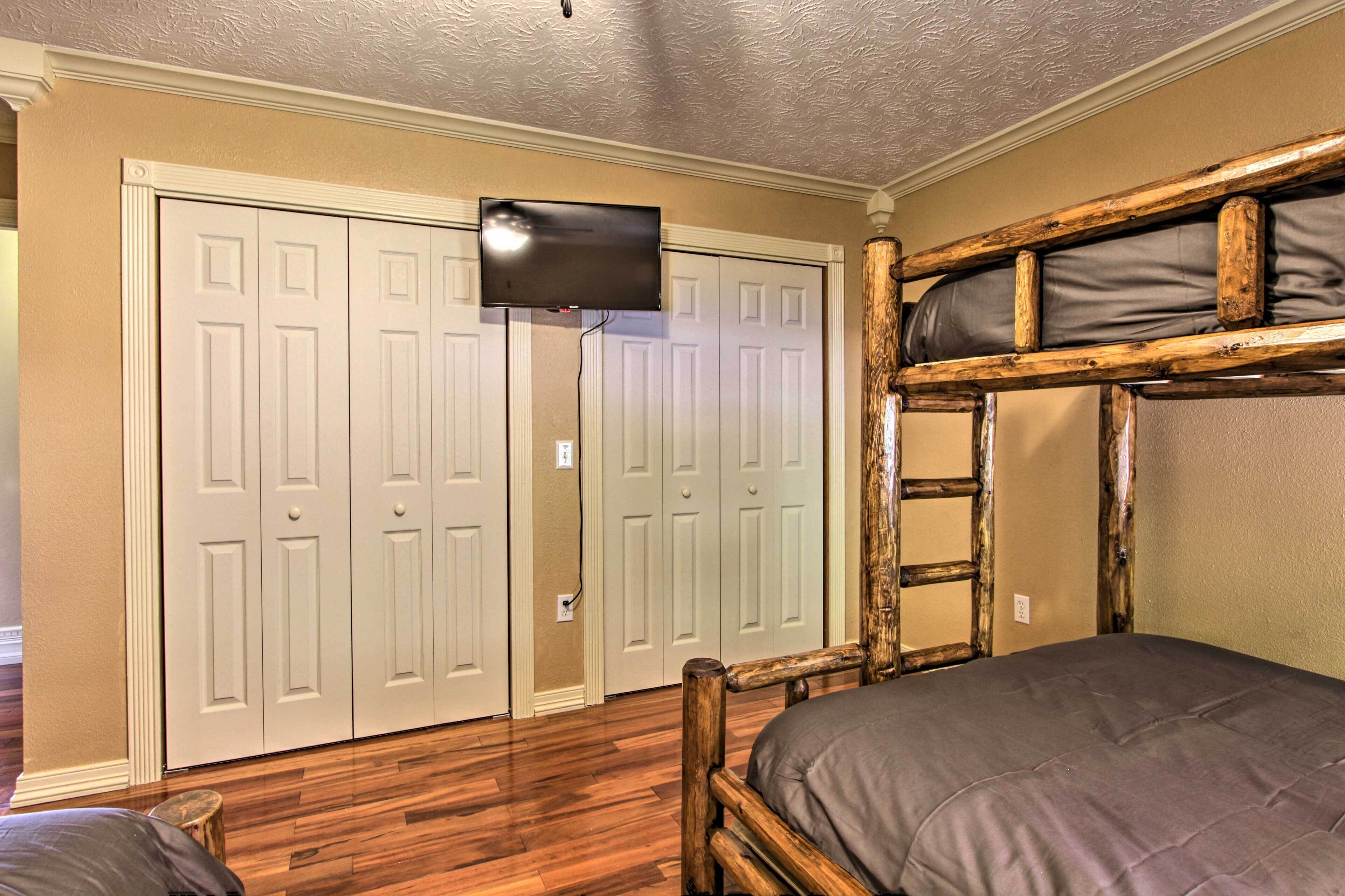A bedroom with two wooden bunk beds, a television mounted on the wall, and a set of double doors in the background.