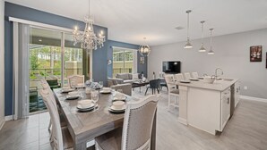 Une cuisine moderne dotée d’un îlot central, un coin repas avec une grande table pouvant accueillir six personnes, et un espace salon avec un canapé et un téléviseur.