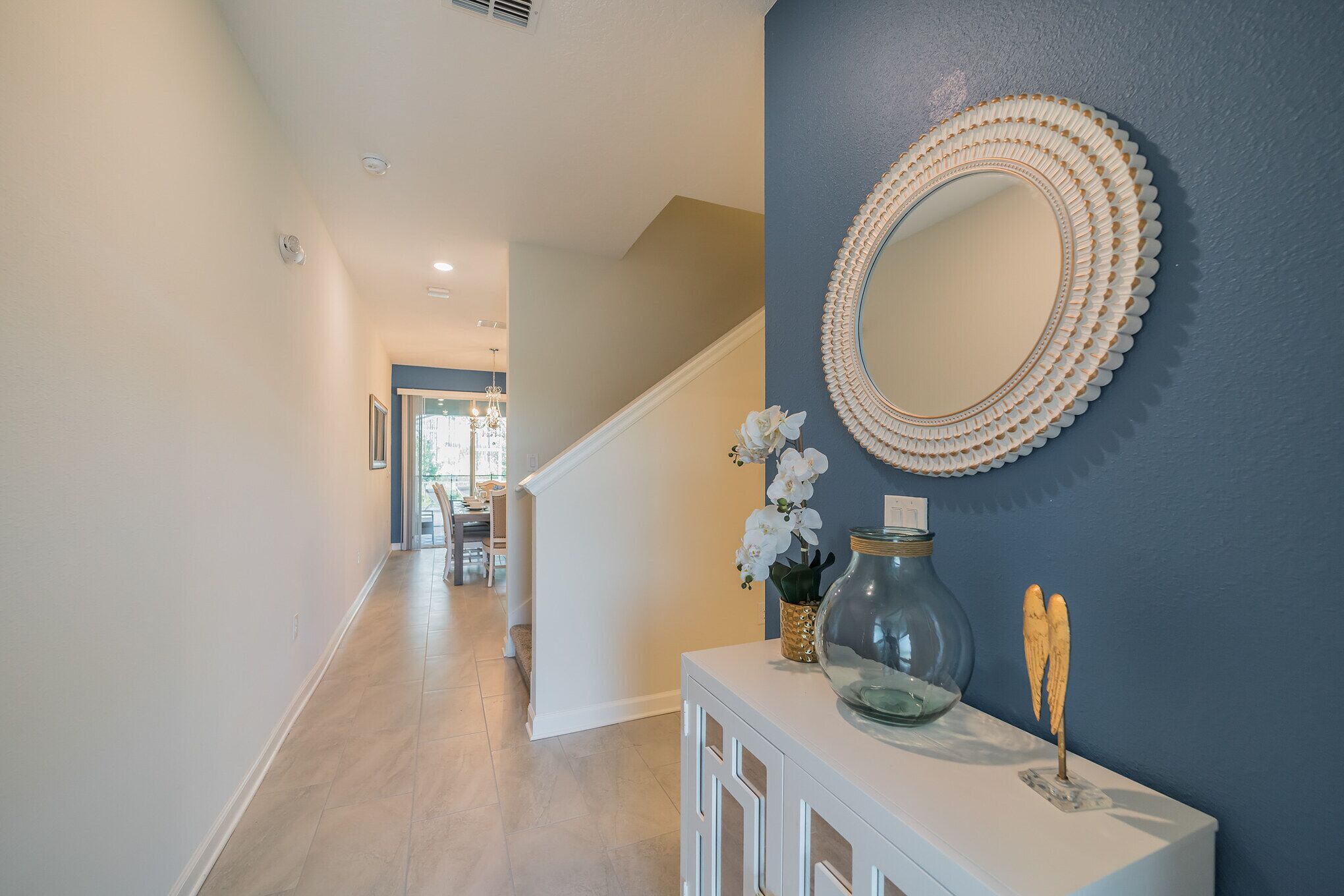A hallway with a staircase, a decorative mirror, and a vase with flowers.