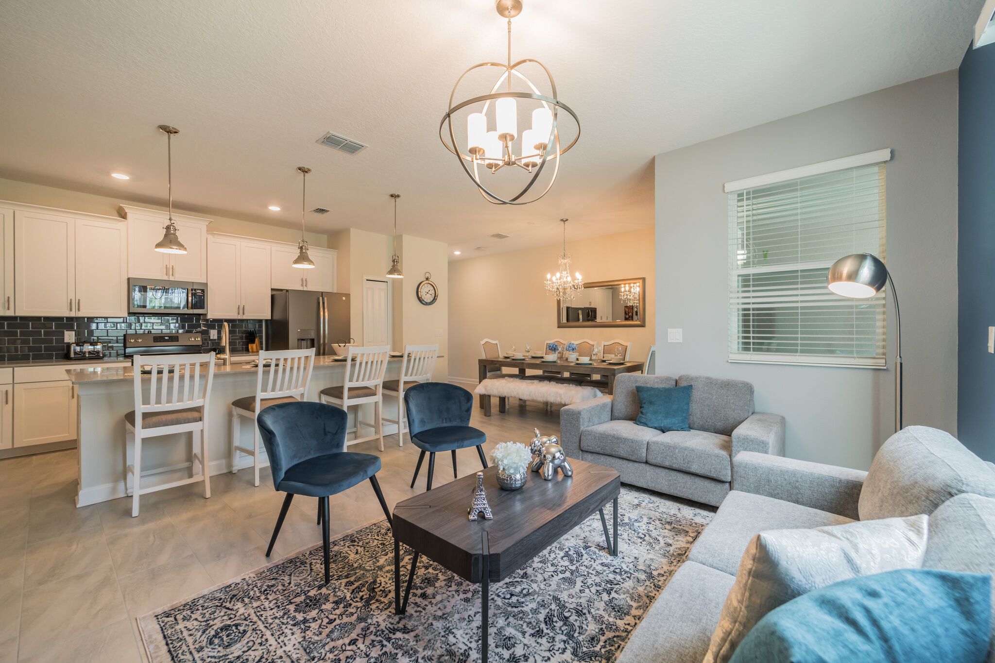 A modern kitchen with white cabinets, a central island, and a dining area with chairs and a table.