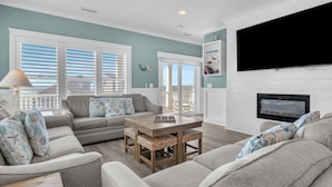 A living room with a grey sofa, a coffee table, and a flat-screen TV mounted on the wall. - Luna's: Amazing Ocean View House with Pool, Spa, Elevator and Electric Car Charg (Oak Island)