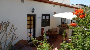 A white building with a tiled roof, a door, and a window. There is a table and chairs outside, and a sign on the wall. - Calma, quiet studio with sea view terrace overlooking the pool (Las Zocas)