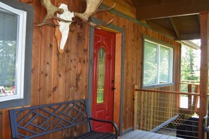 A wooden cabin with a red door, a bench, and a large antler mounted on the wall.