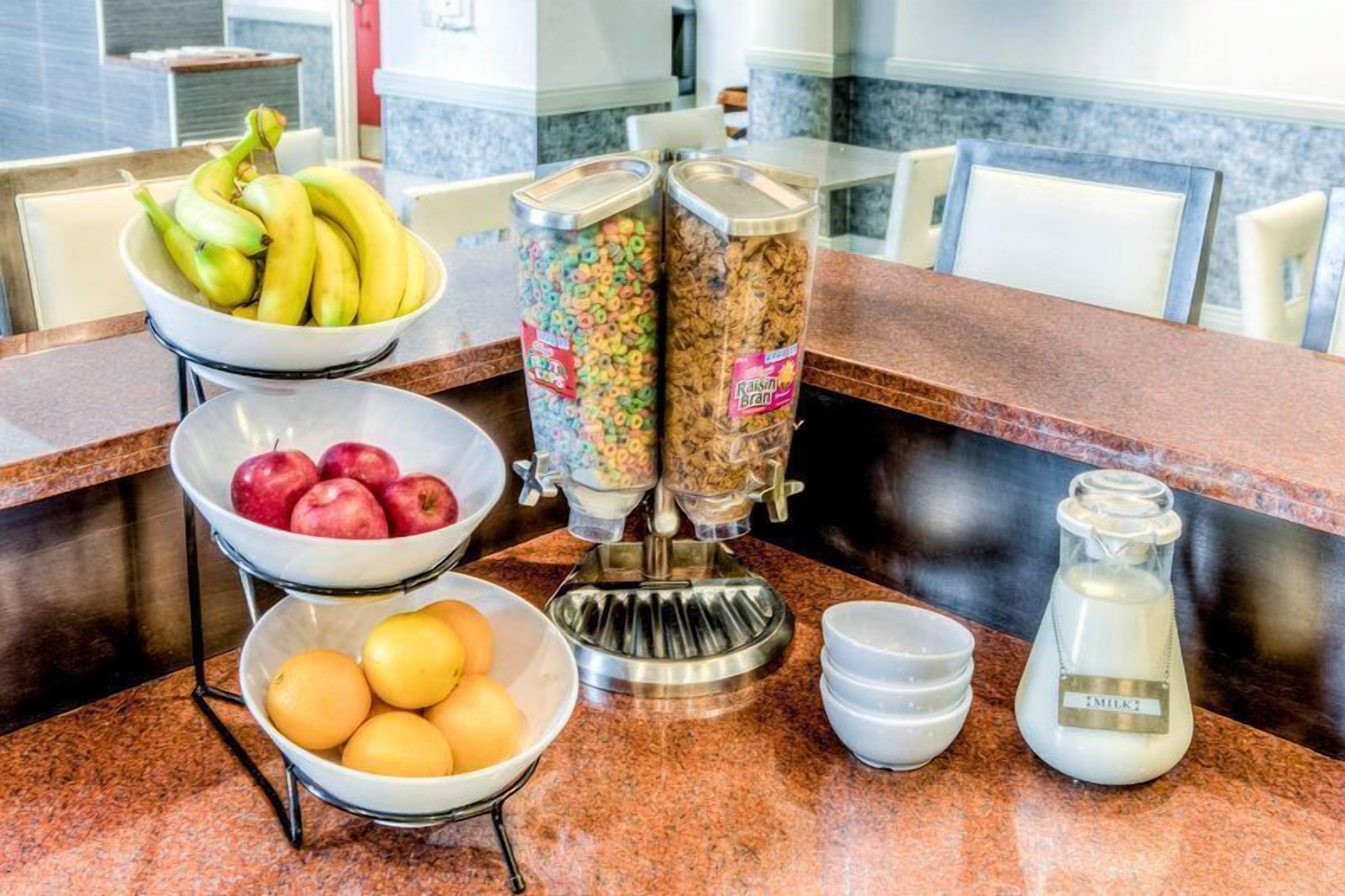A breakfast bar with bowls of fruit, cereal dispensers, and a milk pitcher.
