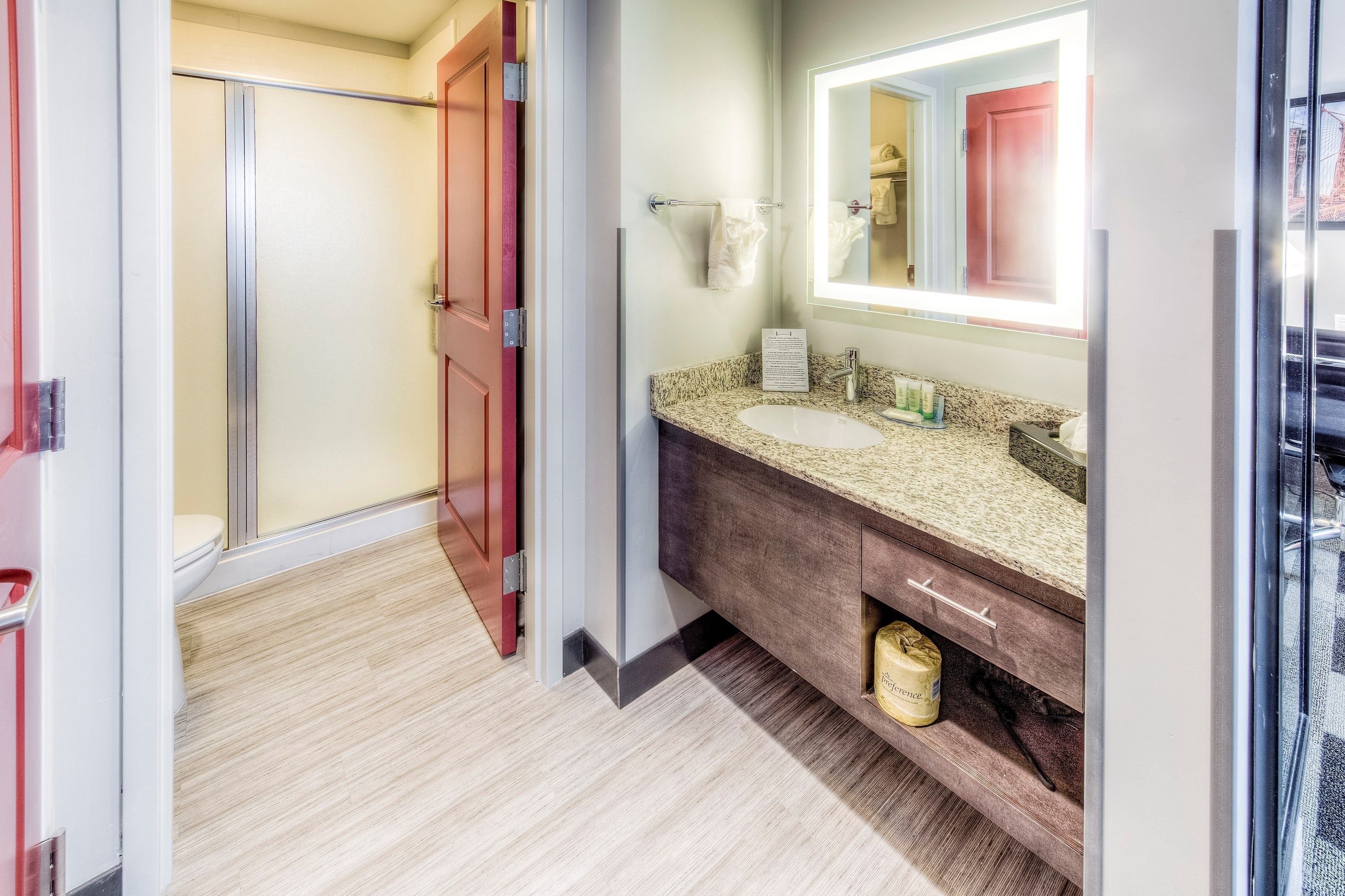Une salle de bain moderne équipée d’une douche, d’un lavabo avec un plan de travail en granit et d’un miroir avec un éclairage au-dessus.