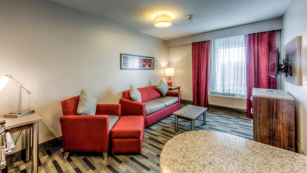 Hotellihuone, jossa on punainen sohva, pieni pöytä, lamppu, televisio ja ikkuna, jossa on punaiset verhot.