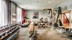Une salle de sport équipée de tapis de course, d’haltères, de bancs et d’appareils de musculation.
