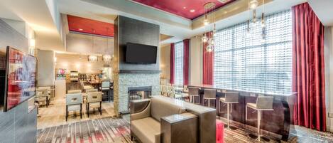 A modern hotel lobby with a seating area, a bar, and a fireplace.