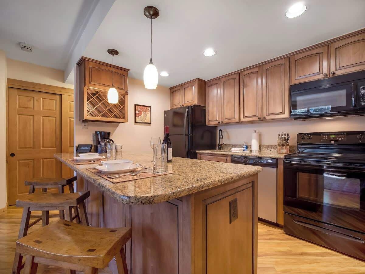 A kitchen with wooden cabinets, a granite countertop, a black refrigerator, a stove, and pendant lighting.