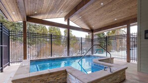Une piscine extérieure avec des marches en pierre et un plafond en bois, entourée d’une clôture en métal noir.