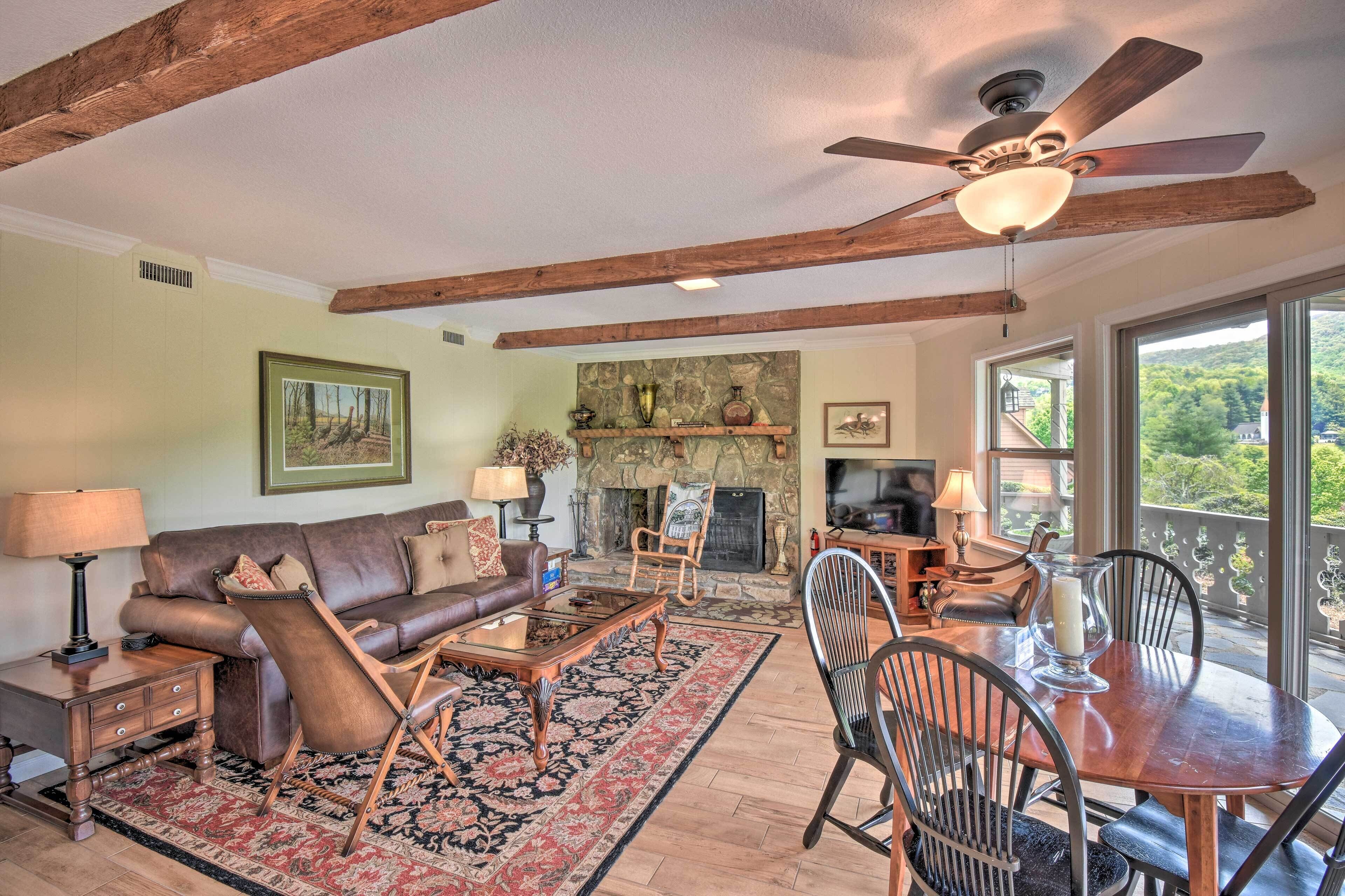 A spacious living room with a fireplace, wooden beams, a large window, and a dining area.