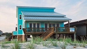 A two-story beach house with a wooden deck and a sign indicating a coffee shop. - Out Of Office: Dog-friendly, Oceanfront Home on West Beach with Corn Hole and Ho (Oak Island)