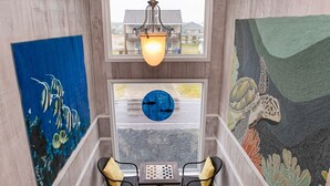 A staircase with a wooden finish, a chandelier, a table with chairs, and two large wall paintings. - Out Of Office: Dog-friendly, Oceanfront Home on West Beach with Corn Hole and Ho (Oak Island)