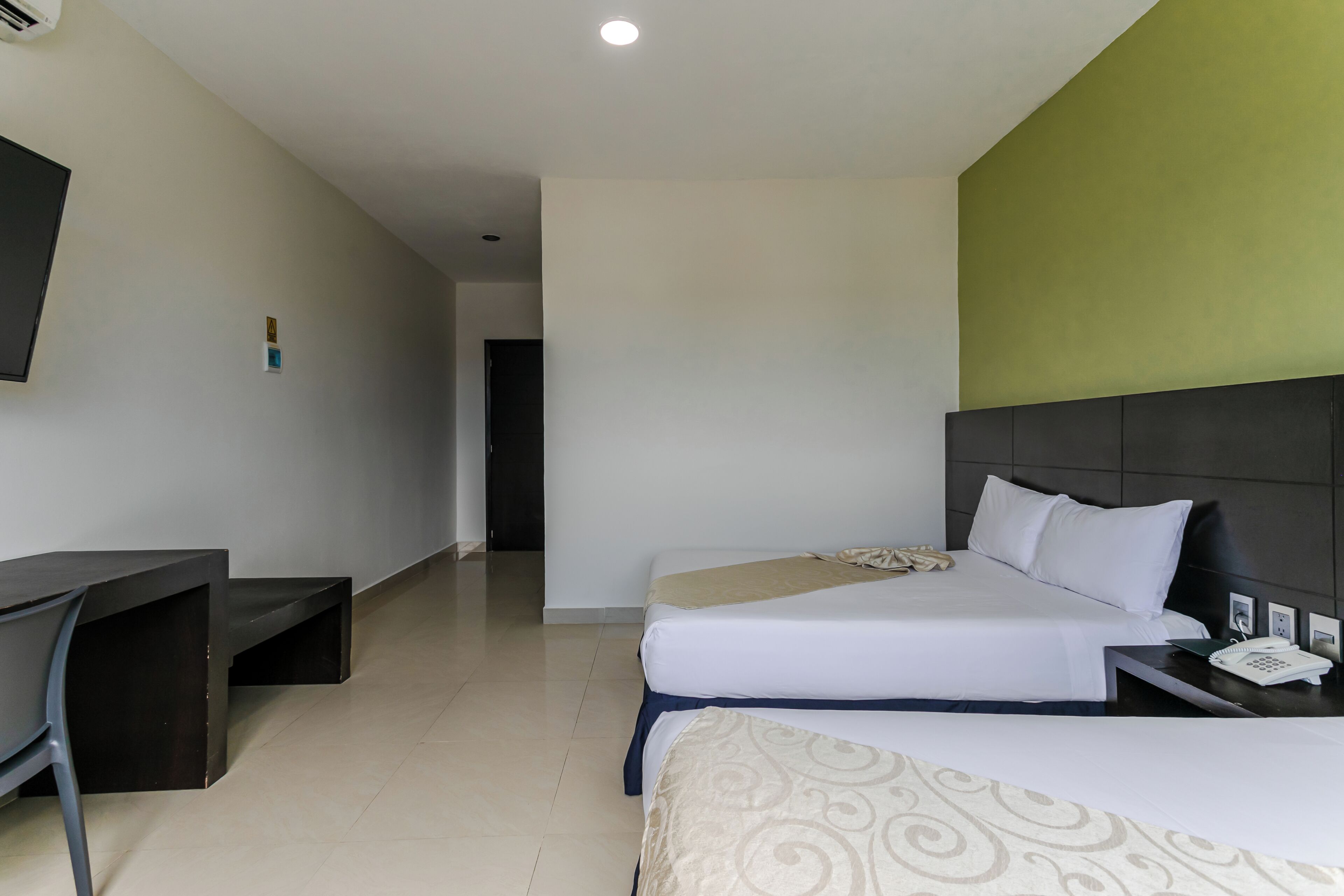 Habitación de hotel con dos camas, un escritorio, una silla y un televisor de pantalla plana.