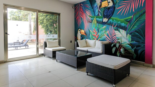 Una sala de estar moderna con una mesa de centro de vidrio, dos sofás y un gran mural tropical en la pared.
