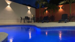 Una piscina con borde de azulejos, rodeada por un muro bajo y palmeras. Hay sillas y una mesa en la zona de la terraza.