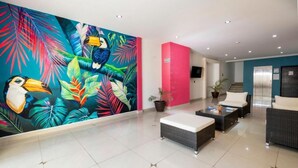Un vestíbulo moderno con un mural vibrante, un área de descanso con mobiliario de mimbre y una escalera que da a un ascensor.