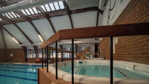 Piscina interior con hidromasaje, terraza de madera y paredes de ladrillo.