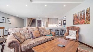 Una sala de estar moderna con sofá, mesa de centro y sillón, una escalera que lleva a una cocina y un comedor.