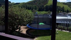 A trampoline in a backyard with a view of green hills and a clear sky.