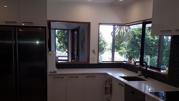 A modern kitchen with white cabinetry, a black refrigerator, and a window providing a view of greenery outside.
