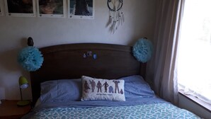A bedroom with a patterned bedspread, a headboard with decorative elements, a wall-mounted dreamcatcher, and a window with curtains.