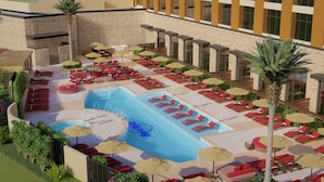 A pool area with sun loungers and umbrellas, surrounded by a stone wall and a building with large windows.