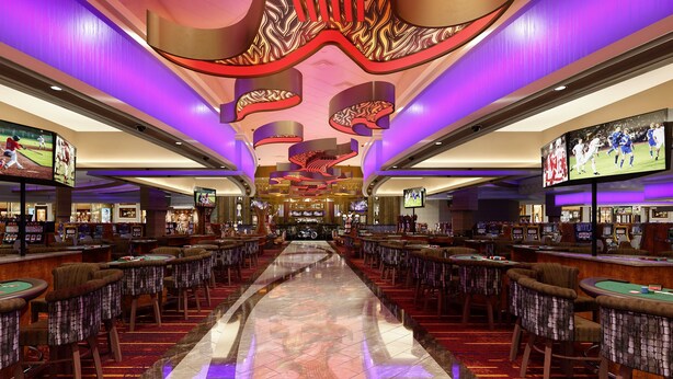 A casino interior with multiple gaming tables, slot machines, and large screens displaying sports events.